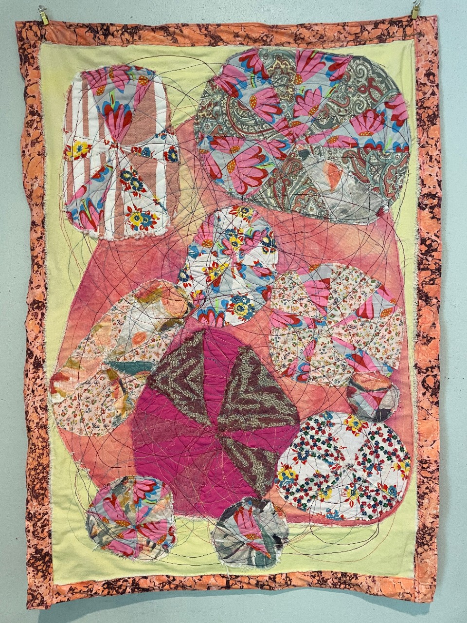 a photo of a quilt made out of several different floral patterns, many of them in shades of pink, displayed hanging on a wall.
