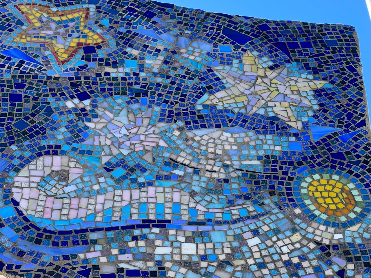 a detailed image of the blue mosaic sculpture depicting a sun, stars of differing sizes, waves and curls, etc.