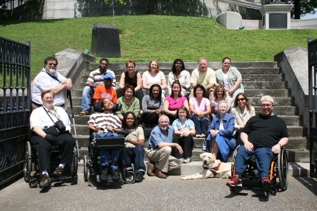 A large banner photo with the article headline shows a diverse group of people, some in wheelchairs, one with a cane, one with a service dog, posing around a set of stone stairs and smiling at the camera.