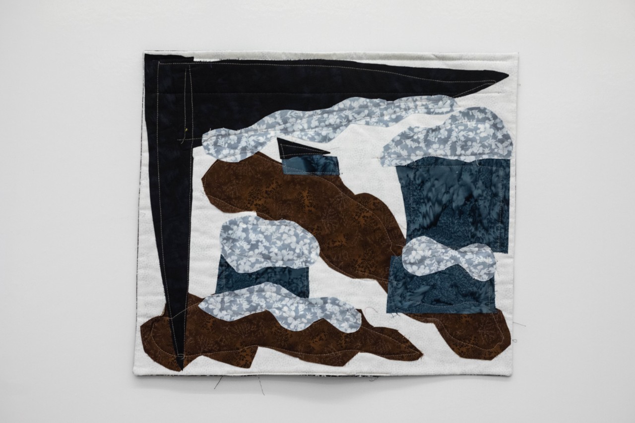 blue and white flowered or patterned fabric with dark blue fabric under it appears to represent rain and flooding, with swaths of brown fabric appearing to represent mud