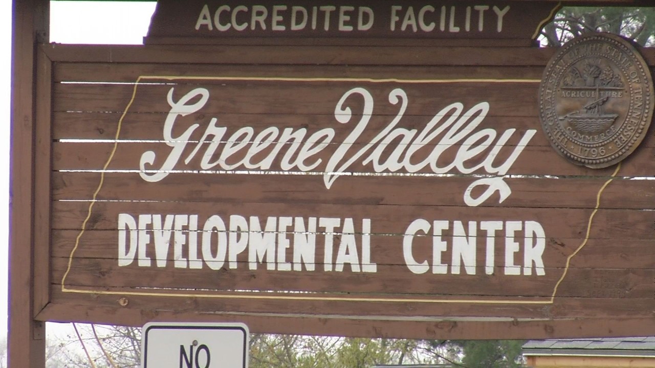 greene valley sign Close-up of a weathered wooden entry sign for “Greene Valley Developmental Center,” trimmed in white paint, with the Tennessee state seal mounted at the top right.