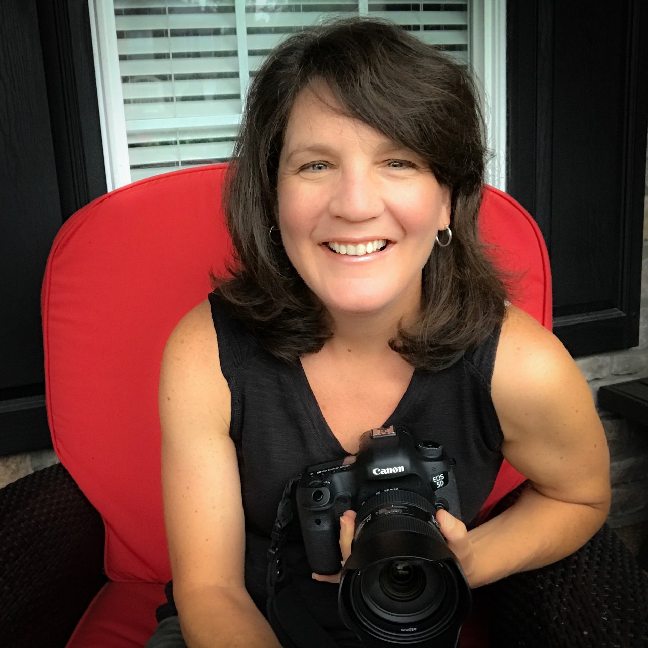 self-portrait of the article author and photographer, Jen Vogus. She is seated in a red chair holding very large camera with a big lens.