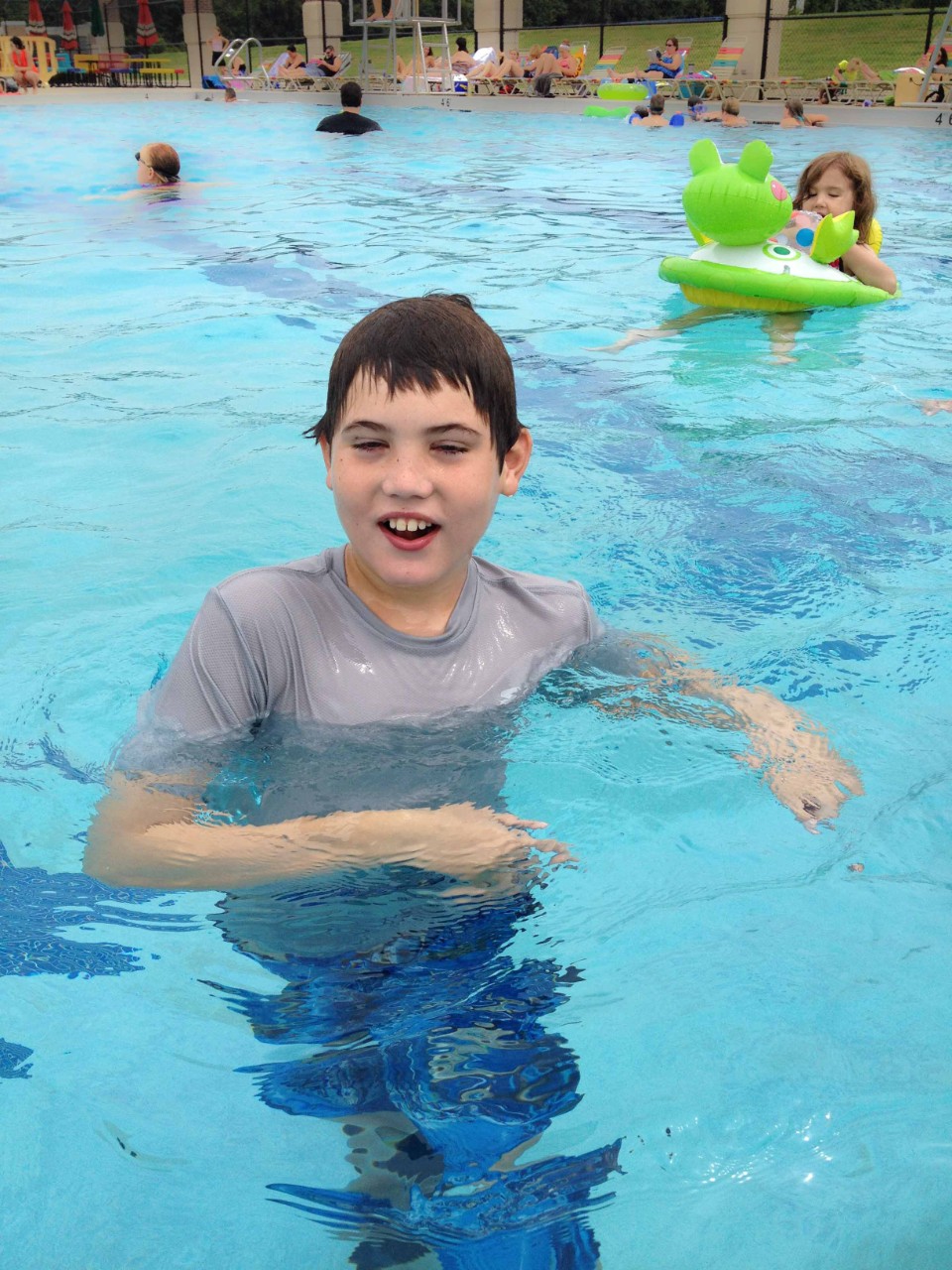 a young boy is swimming in a big public pool. He is obviously very happy to be in the water.