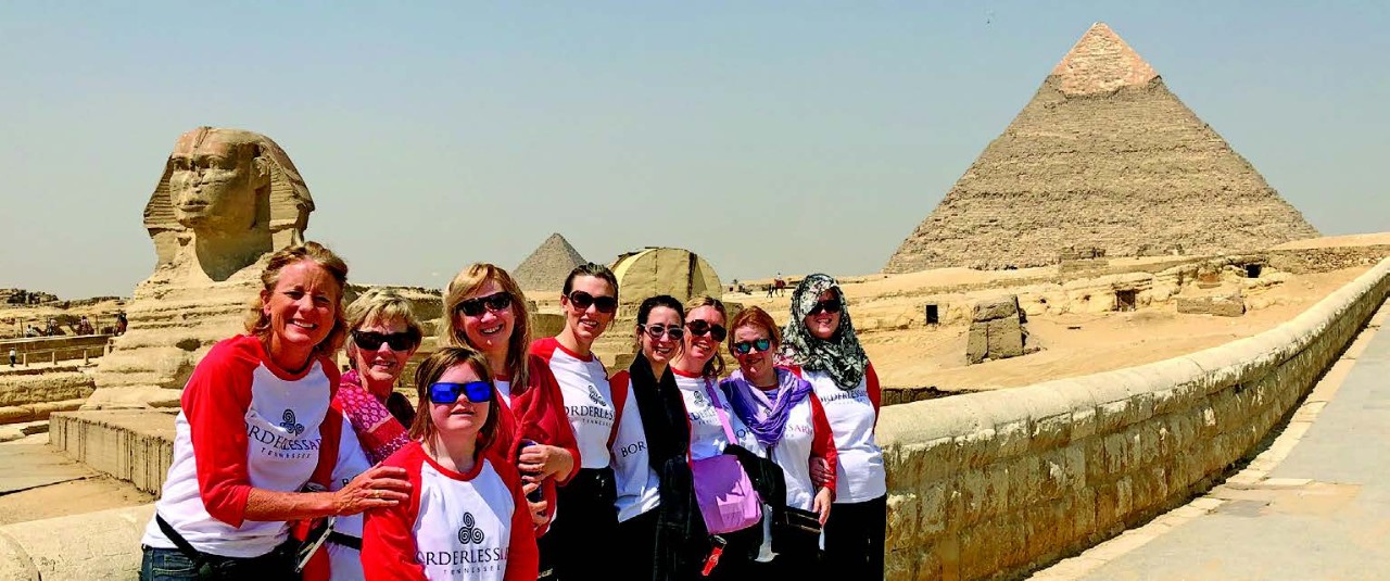 nine women of various ages leaning against a short wall. In the background you can see Egyptian monuments