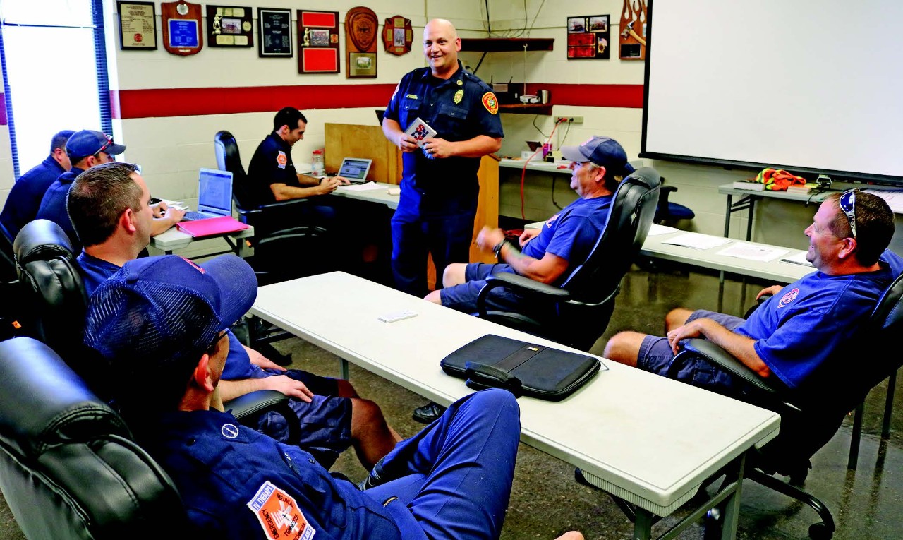 a meeting room with a standing firefighter training seven seated firefighters. The trainer is Captain Phillips, and he is describing the SNAP training, which is described in the article.