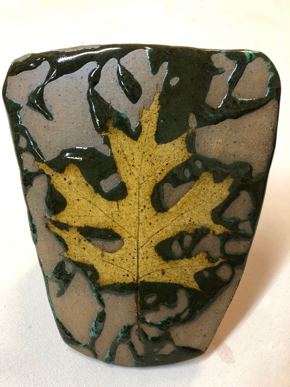 ceramic piece that features a brown, speckled leaf in the middle of a black and brown background