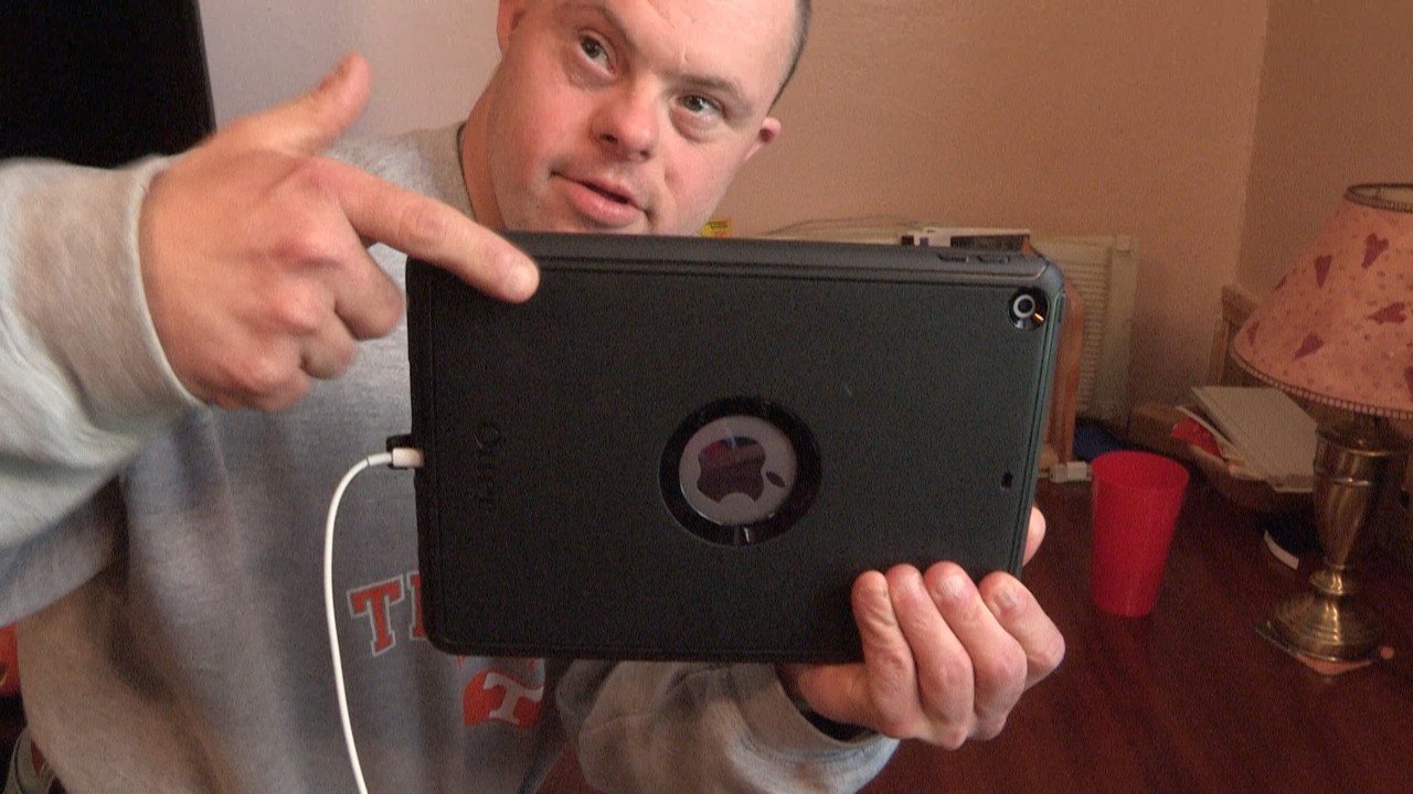Brad is pointing to a black iPad that has a white power cord attached to it