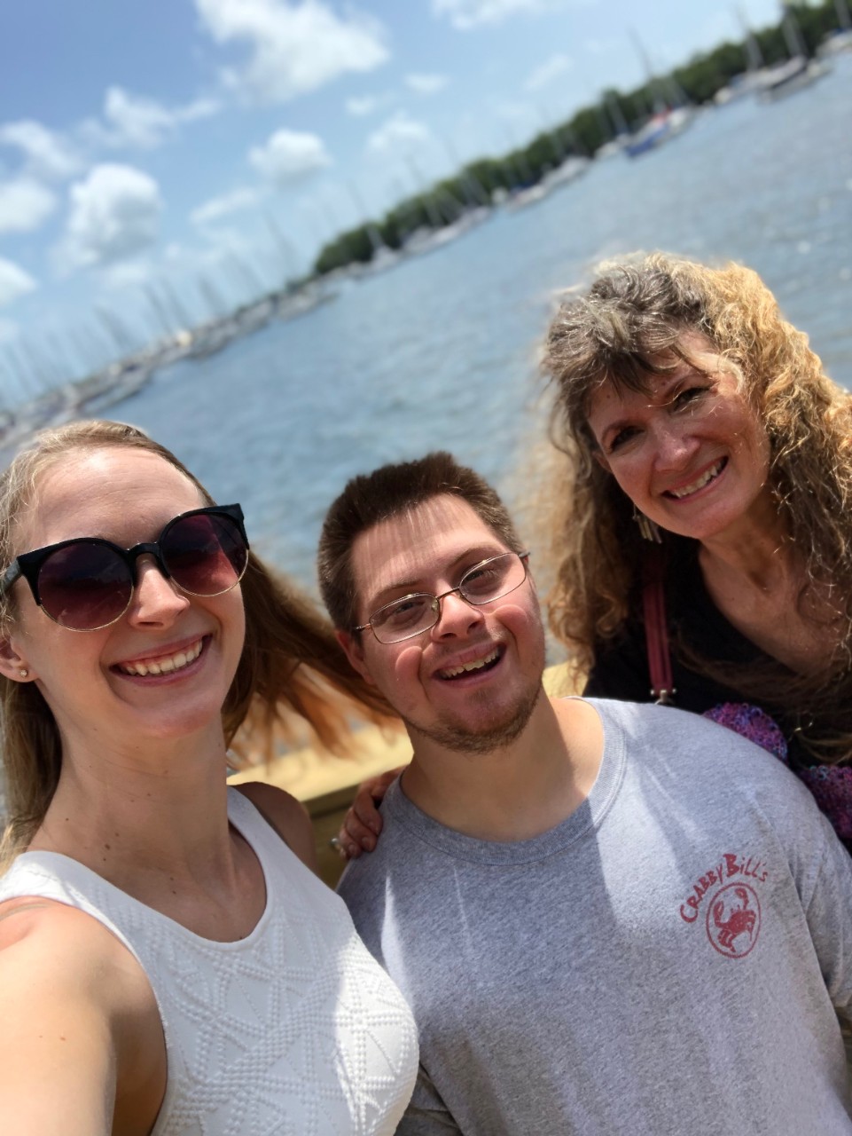 a young woman, a young man with Down syndrome and a mother take a selfie in front of the ocean; all are smiling and dressed in summerwear