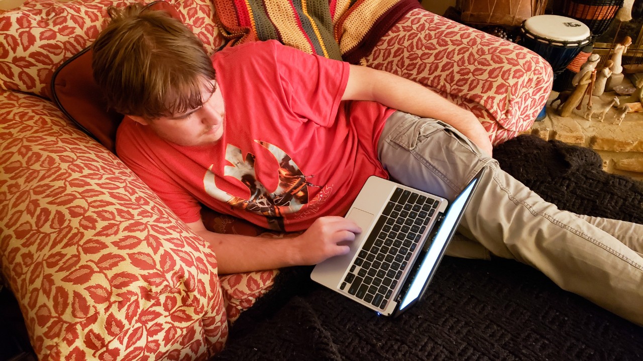 The photo shows a young man, in a red shirt, sitting in a chair with his laptop. The caption reads, “Bernie finds calm in a noisy living room with guests.” 