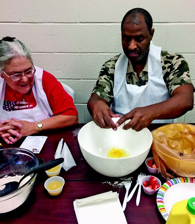 a man and a woman with aprons are working on a recipe that involves cracking an egg into a bowl