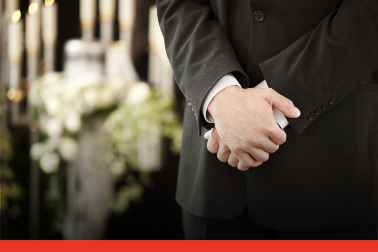 Crossed hands of man in a suit in front of candles and flowers