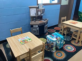 Photo of child visitation area with child tables and chairs, rug, kitchen play set, books, and building blocks.