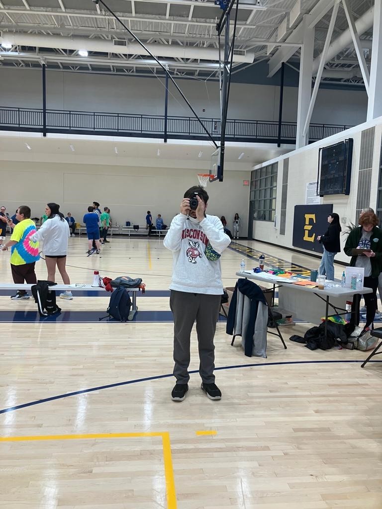 A man in a basketball arena holding up a dslr camera to his face