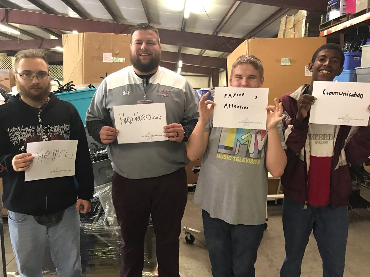 4 people standing in a warehouse holding signs 