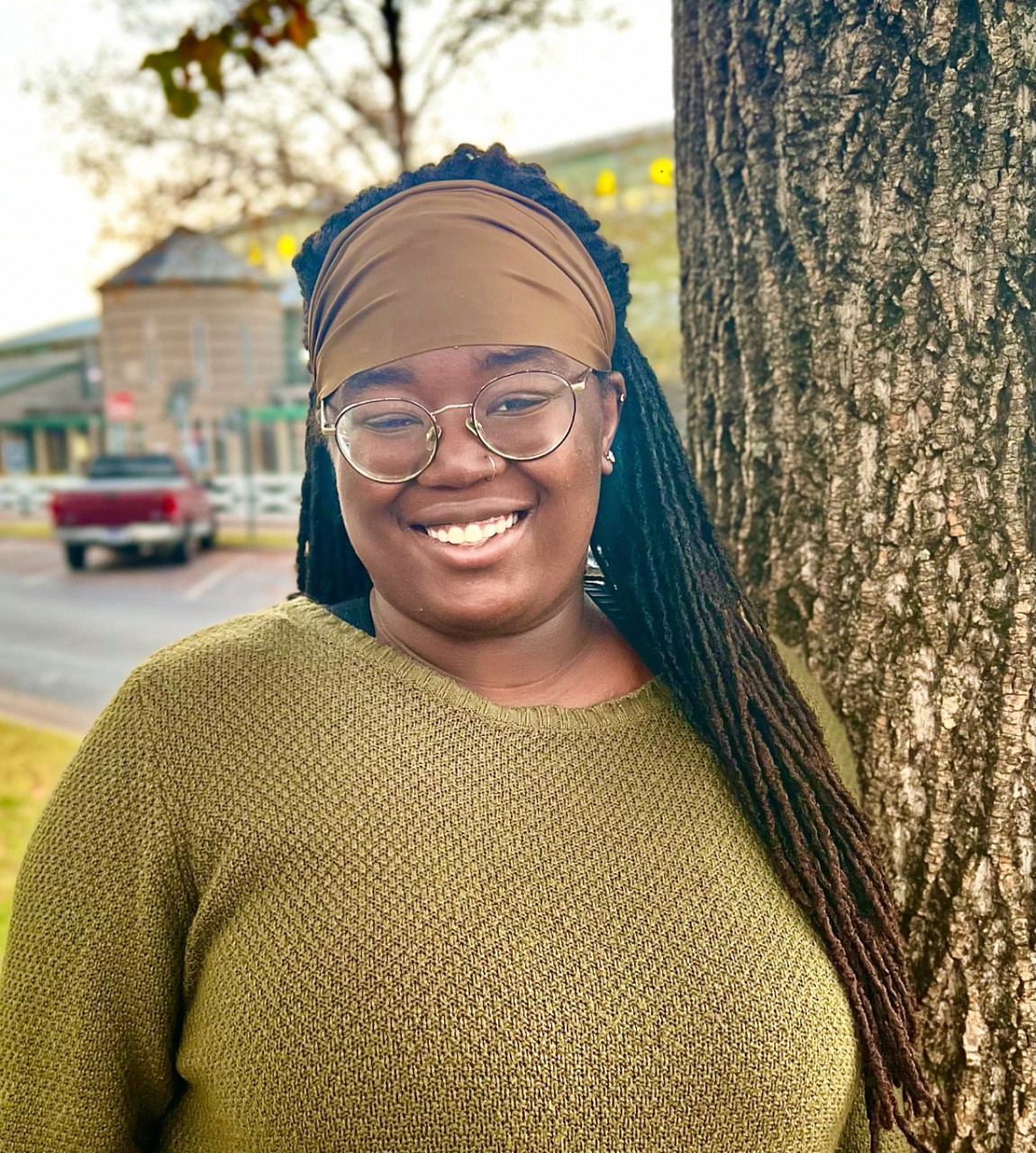 dark complected woman wearing round glasses and smiling big next to a tree