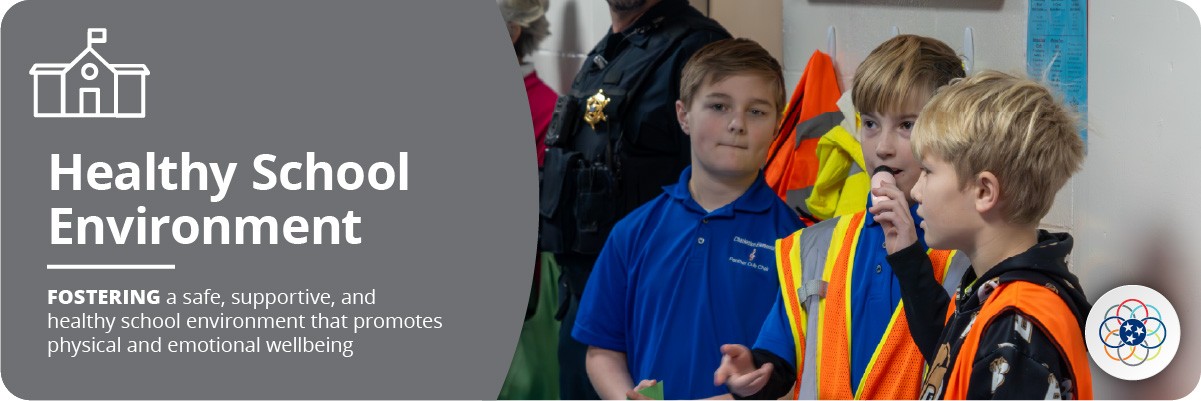 Healthy School Environment Headline: Healthy School Environment Sub-headline: FOSTERING a safe, supportive, and healthy school environment that promotes physical and emotional wellbeing Icon: School building Image: Three boys standing together, two of whom are wearing orange and yellow safety vests, with an officer in the background.