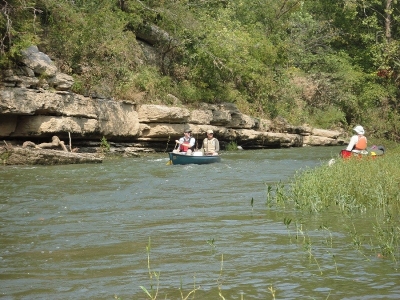 Two people in a canoe navigating along a rock bluff on the Duck River