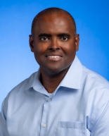 Photo of a young black man wearing a light blue button down shirt.