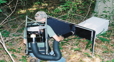 Person handling mosquito surveillance equipment placed on the ground in a wooded area.