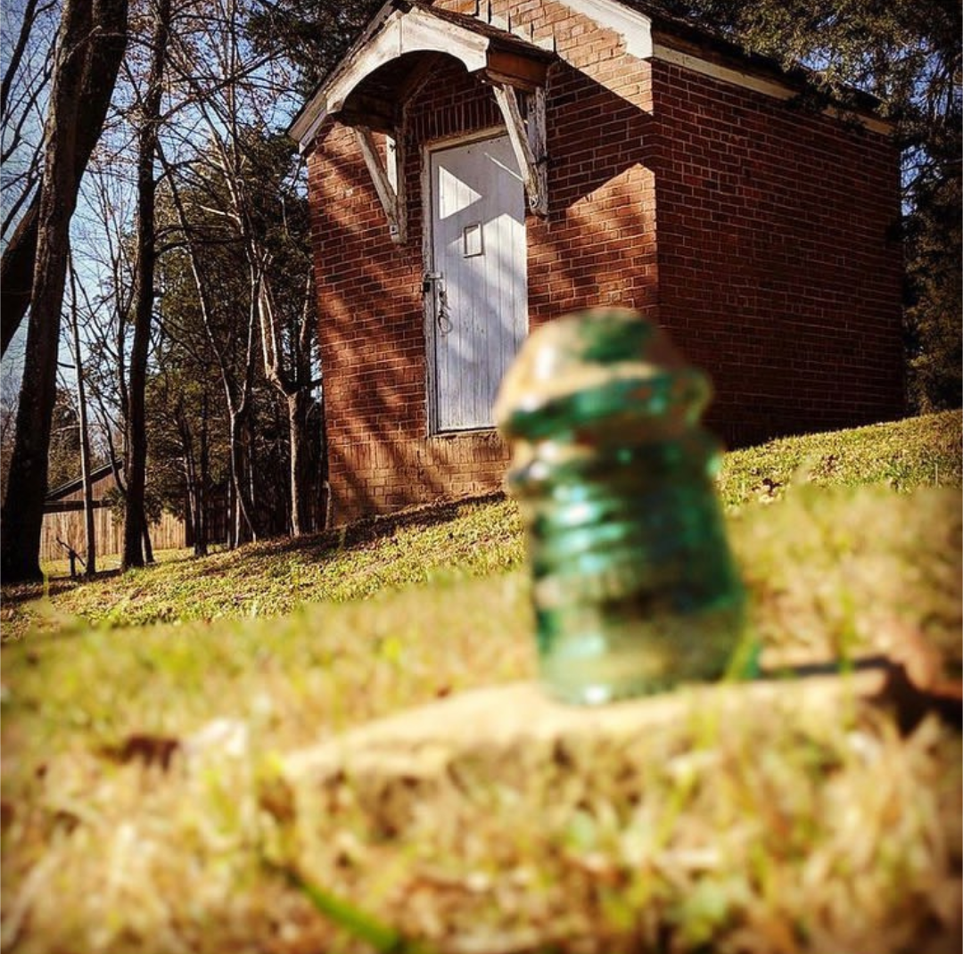 This is the Telephone Switchboard Office at Port Royal State Historic Park, with an early 20th century insulator in the foreground. The switchboard office was constructed in the 1920’s. A green insulator in the foreground with a small brick building in the background