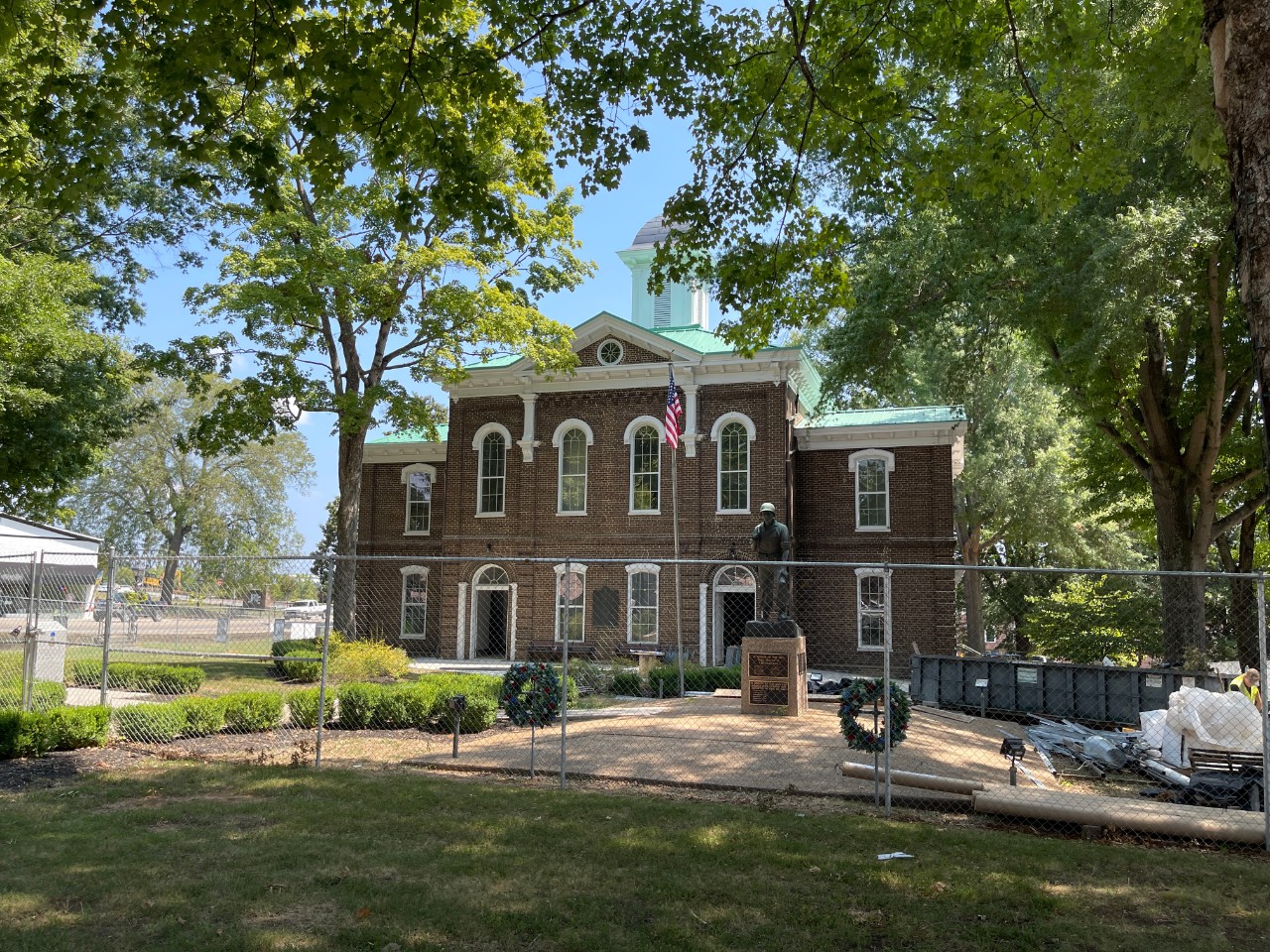 Image of a courthouse with a fence around the building. A statue of a man and an American flag are in the foreground