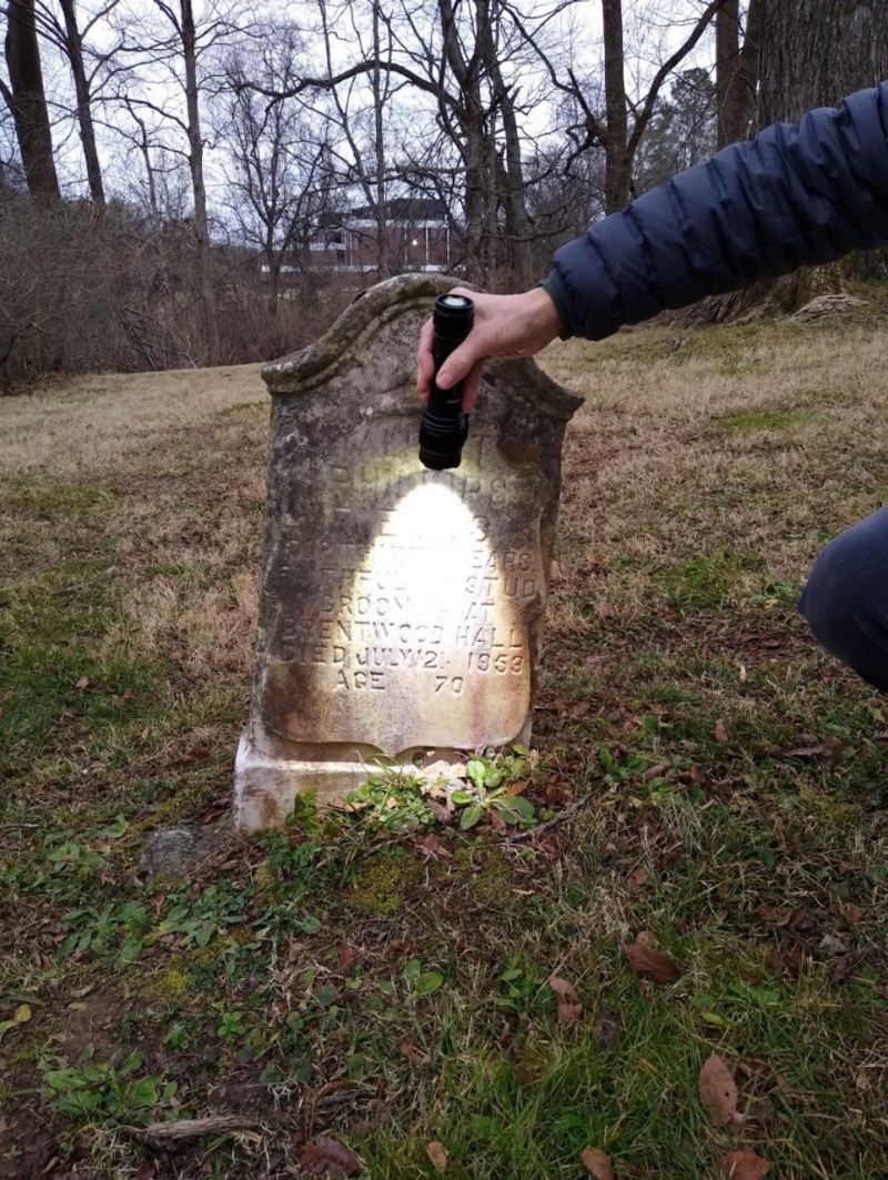 Image of someone shining a flashlight on a headstone in the William Ewing Family Cemetery
