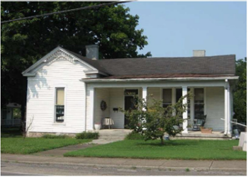 Image of a white Victorian style home with a bush in front of it