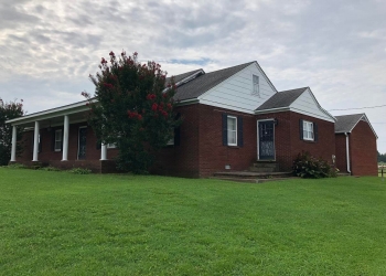 Image of a brick home with white columns. There is a tree with pink flowers in front of the home.