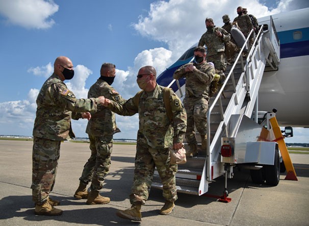 Soldiers coming off a commercial plane being greeted by Generals