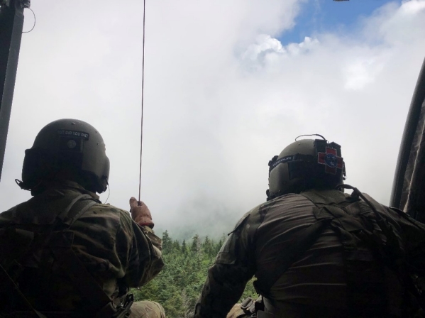 Sgt. Daniel Mills, the aircraft crew chief, operates the aircraft rescue hoist while Sgt. 1st Class Giovanni DeZuani, the aircraft flight paramedic, monitors the approaching cloud layer while hoisting a hiker with a life-threatening illness into the helicopter on Mount LeConte at the Great Smoky Mountain National Park area, July 19. (Photo from the Tennessee National Guard)