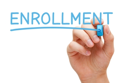 hand writing the word enrollment with a blue marker