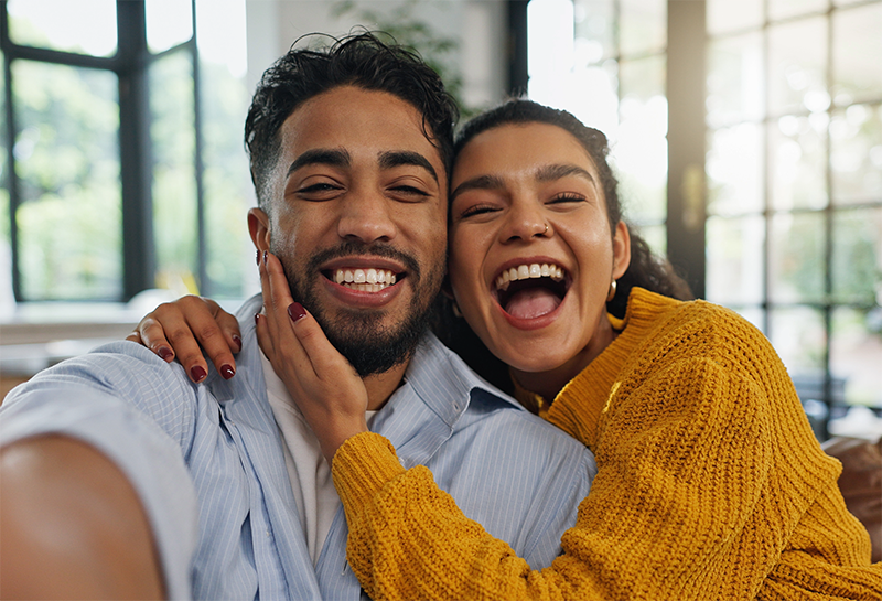 Man in the foreground working on a computer with a woman and two children in the background sitting on a couch