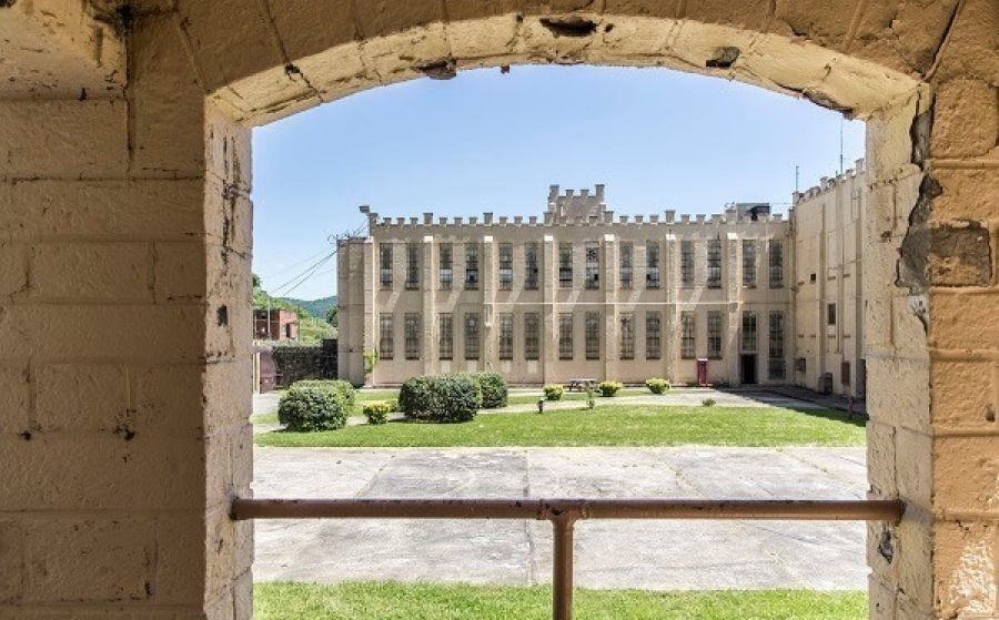 A historic stone building is viewed through an arched opening, overlooking a grassy courtyard.