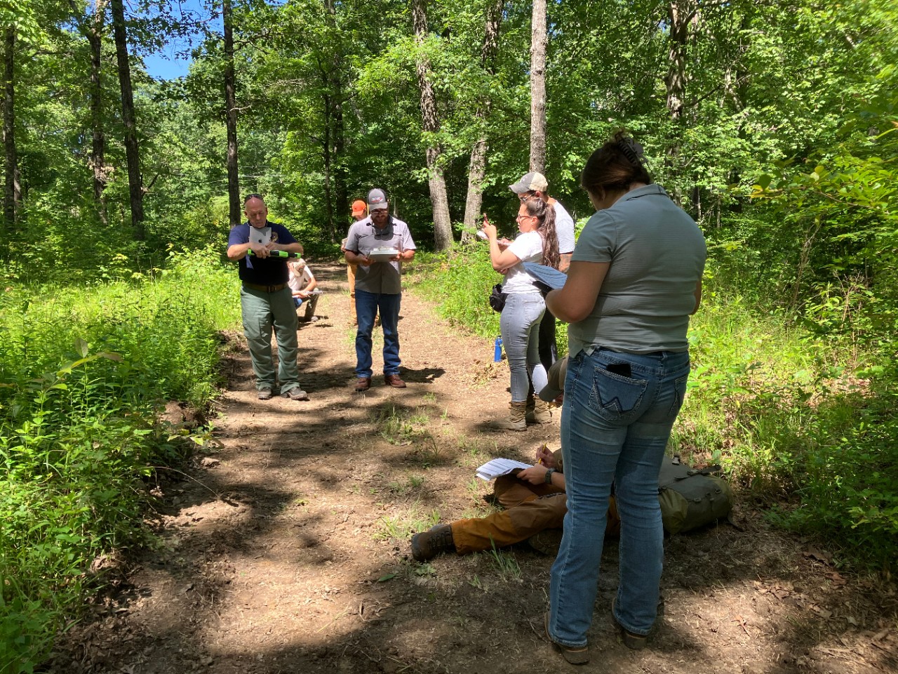 A group of adults taking notes in a forested area during a field day exercise