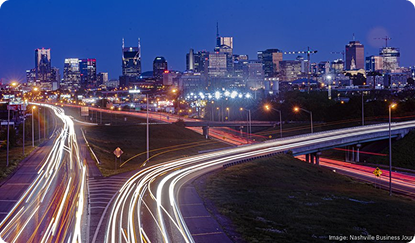 Photo of car headlights on a highway into a city skyline at night