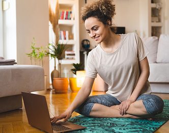 a woman sitting on the floor on a yoga mat looking at her laptop