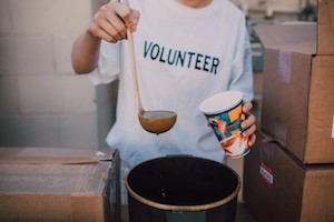 Close-up of a person putting soup into a cup. The person is wearing a volunteer shirt.