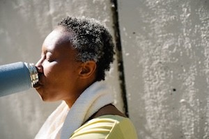 A woman is leaning up against a wall drinking from a water tumbler