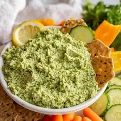 a bowl of edamame dip with crackers on the side and a lemon wedge