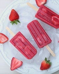 Homemade Strawberry Popsicles overhead view of three strawberry popsicles on a platter with fresh strawberries scattered around