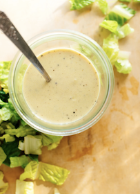 Overhead view of a cup with honey mustard salad dressing in it. Around the cup is romaine lettuce.