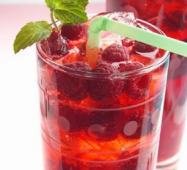 a red raspberry drink with fresh berries and a mint garnish in a clear glass and a straw