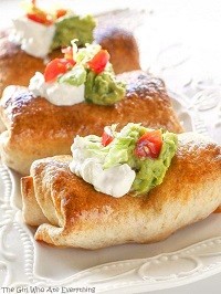 three chimichangas on a plate, topped with sour cream and guacamole