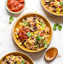 Beans and rice with corn and salsa on a few plates with a side of salsa