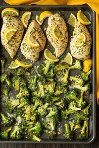 A baking pan with roasted chicken, broccoli and lemon