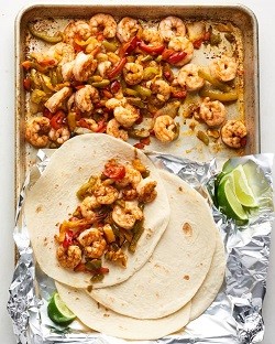 A baking sheet with shrimp, flour tortillas and lemon wedges