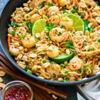 a pan of shrimp pad thai with lime wedges