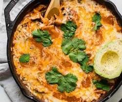 Cheesy enchiladas in a skillet with half an avocado on top
