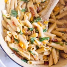 Tuscan Chicken Pasta in a bowl with a wooden spoon