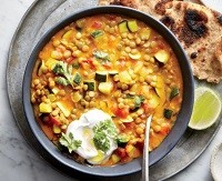 A bowl of curried lentil and vegetable stew with a side of naan